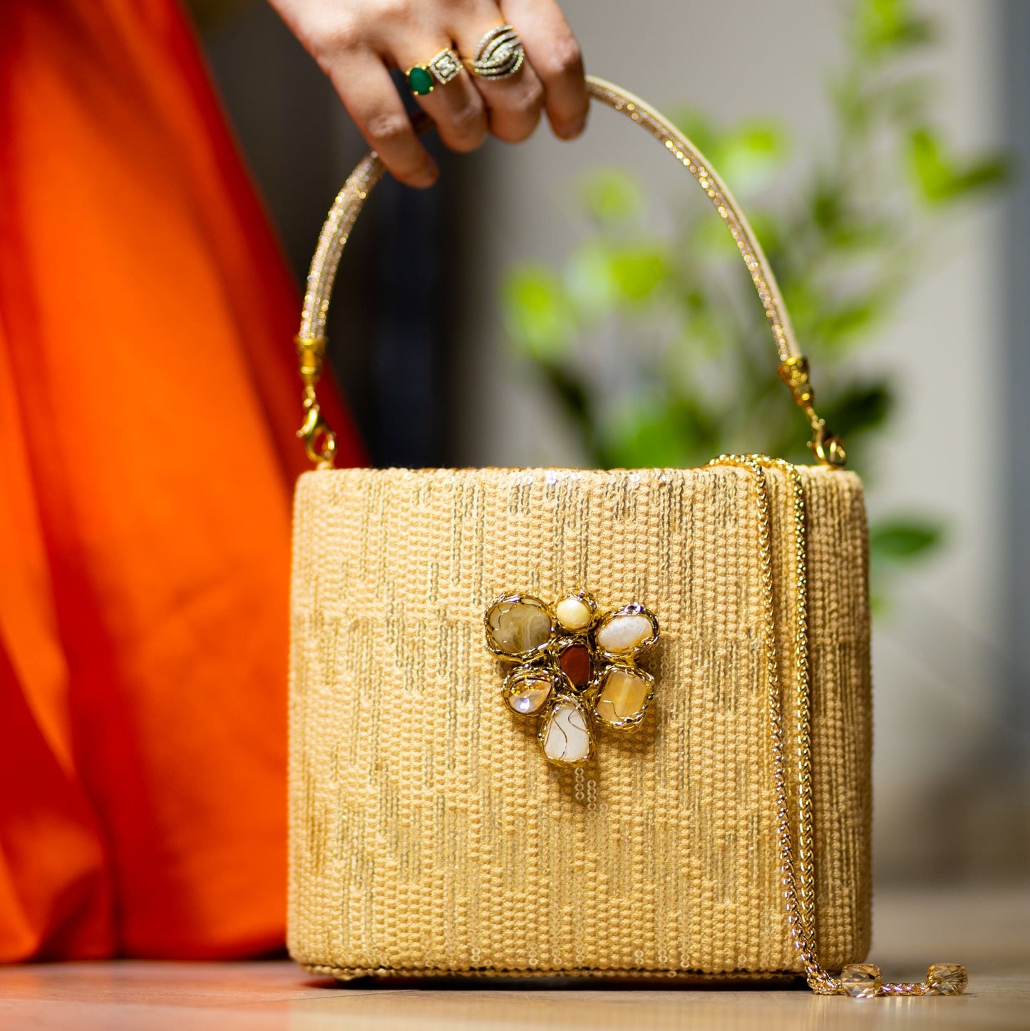 A person holding a gold sequinned clutch with crystal embellishments and a tassel.