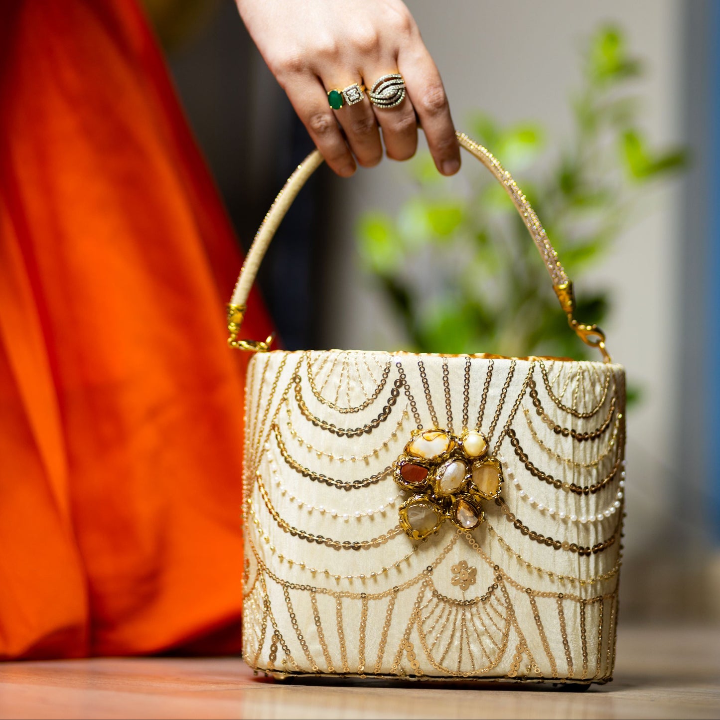 A hand holding a beige and gold colored crystal encrusted pearl clutch with intricate designs and embellishments.