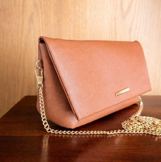 Tan Brown leather handbag with a gold chain on a wooden surface
