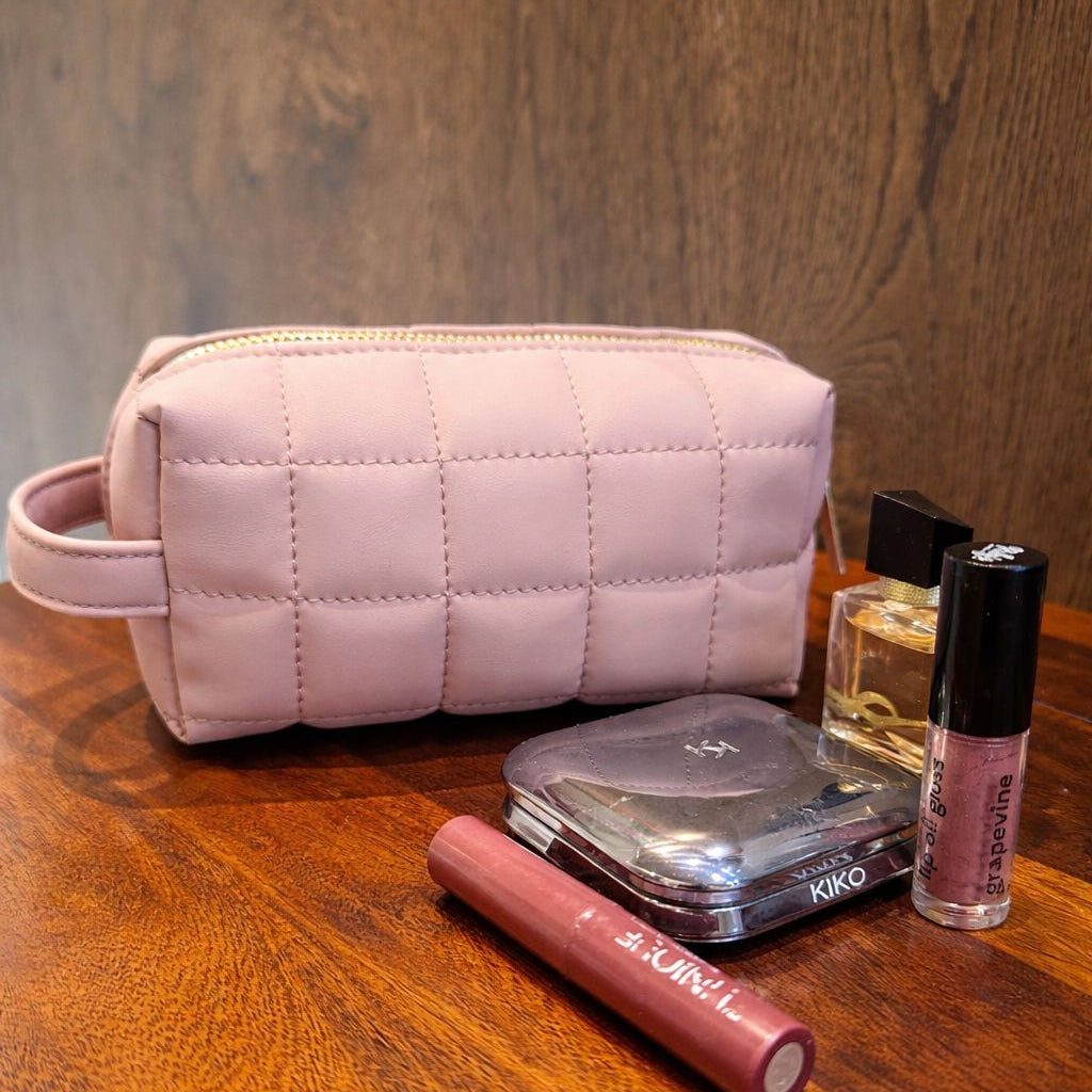 Pink quilted makeup bag with cosmetic items on a wooden surface