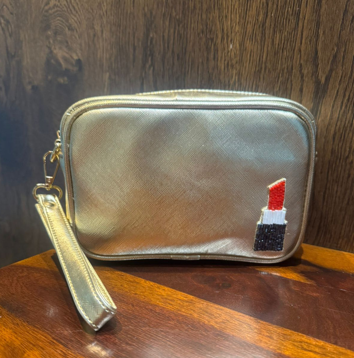 Silver cosmetic bag with a lipstick charm on a wooden surface