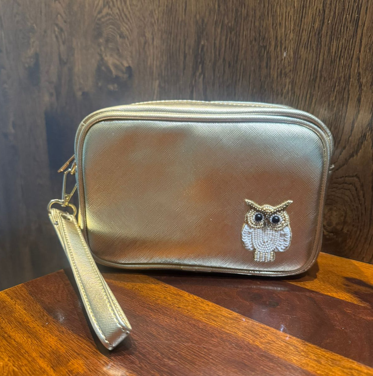 Gold pouch with owl design on a wooden surface